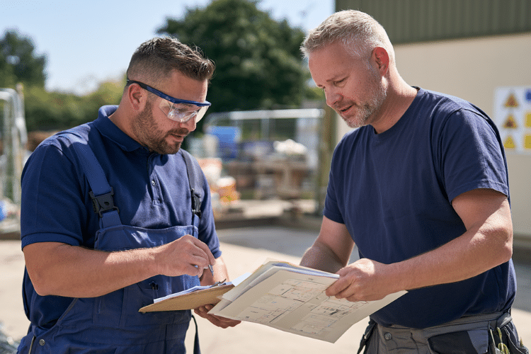 Tradesperson and site supervisor reviewing asbestos risk assessment paperwork outdoors
